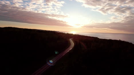 aerial: car driving along empty country road into golden summer sunset