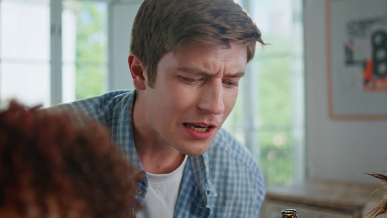 Focused guy drinking beer supporting video gaming friends at home party closeup