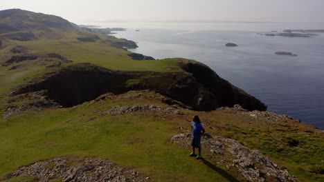 un hombre irlandés con largos paños contempla la naturaleza desde un acantilado cubierto de hierba