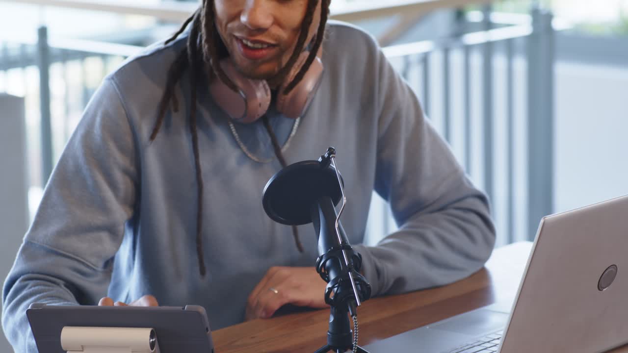 Mid adult man sipping coffee puzzled look recording podcast mic tapping tablet in coworking space
