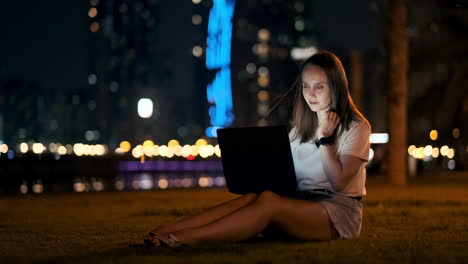 una joven estudiante con una computadora portátil por la noche en la ciudad mirando la pantalla de la computadora y escribiendo con las manos en el teclado. trabajo remoto en internet. la estudiante hace el trabajo. vida nocturna en la ciudad