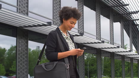 Mujer-De-Negocios-Fuera-Del-Moderno-Edificio-De-Oficinas-Comprobando-Mensajes-En-El-Teléfono-Móvil