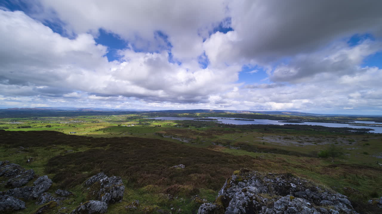Timelapse di un paesaggio rurale con formazione rocciosa in primo piano, colline e lago in lontananza durante una giornata nuvolosa e soleggiata, visto da Carrowkeel, nella contea di Sligo, in Irlanda