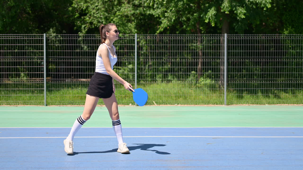 Woman playing pickleball on a blue and green court on a sunny day