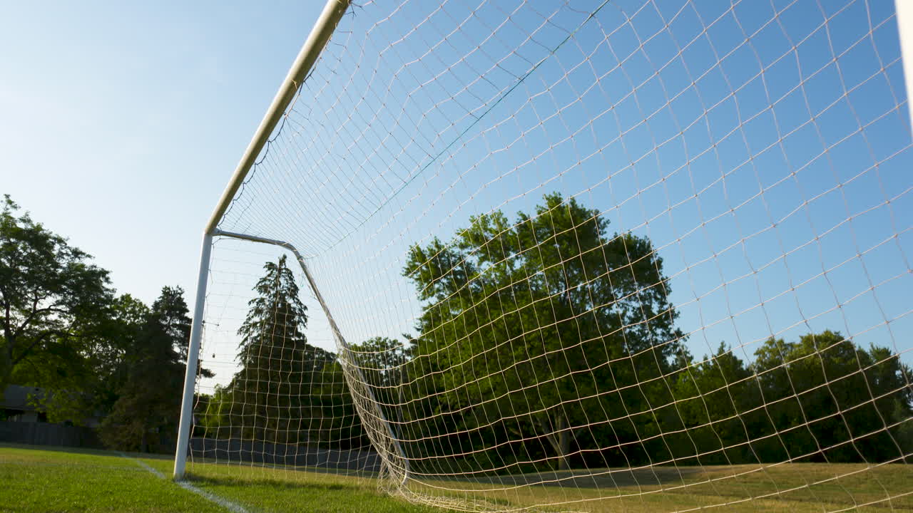 A low angle dolly backwards past a soccer net on a sunny, summer morning