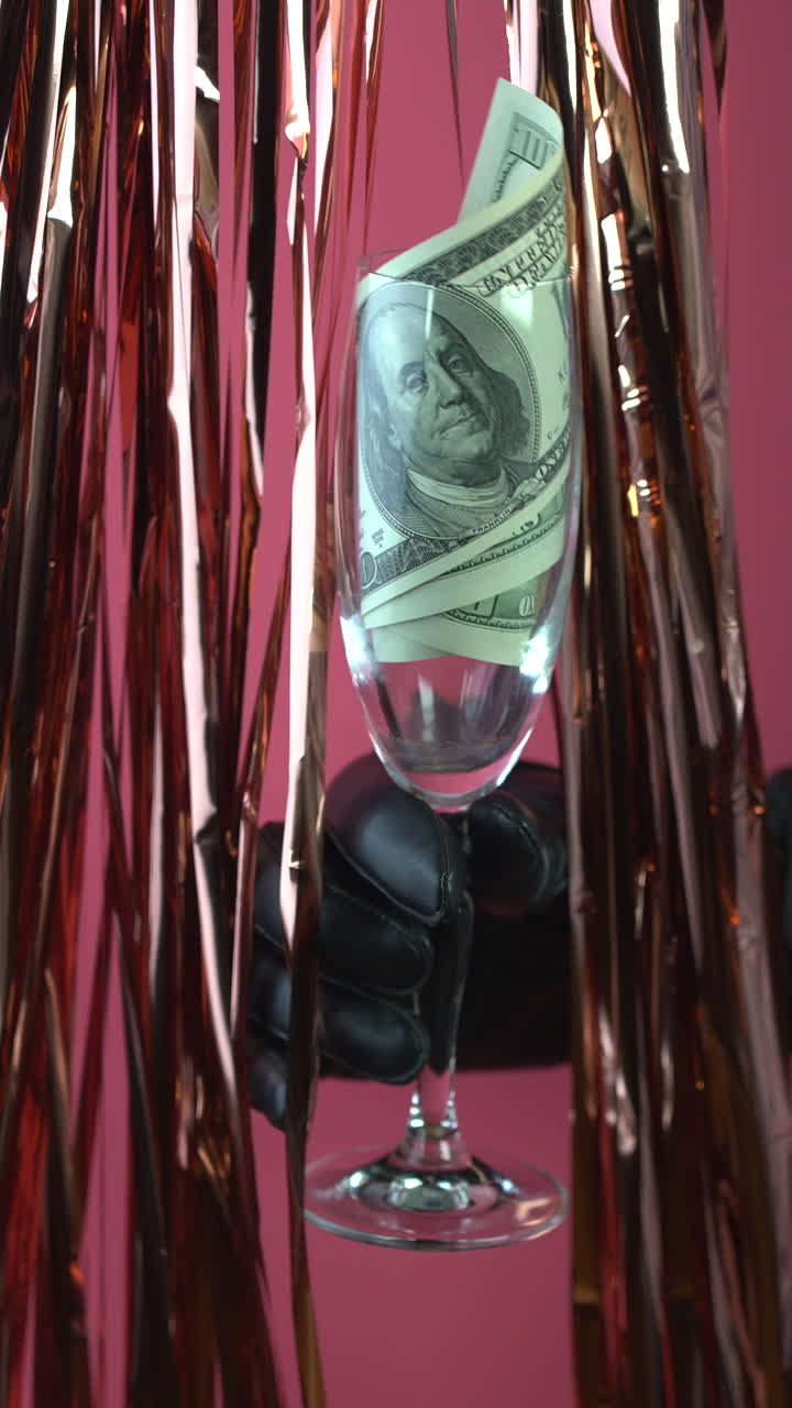 Mano guantata che tiene un calice da champagne con banconote da cento dollari.
