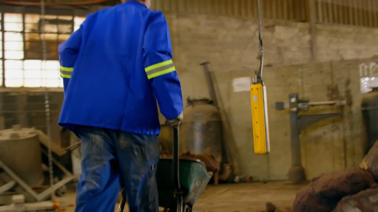 Operaio che spinge una carriola in un'officina di fonderia 4k