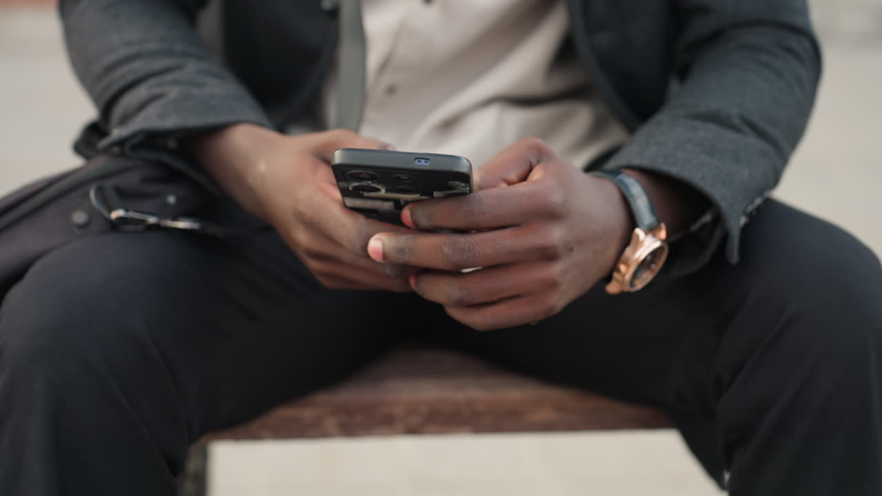 Camera captures chest level view of hands holding smartphone while sitting firmly on wooden art bench, showcasing wrist watch, detailed texture, modern fashion, and human expression of focus
