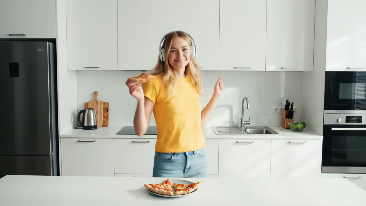 Donna con le cuffie che balla e mangia pizza in cucina