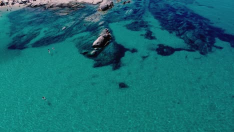 Tourist-standing-on-rock-and-Swimming-clear-water-of-Kavourotrypes-Beach-at-Chalkidiki,-Greece---drone-tilt-up