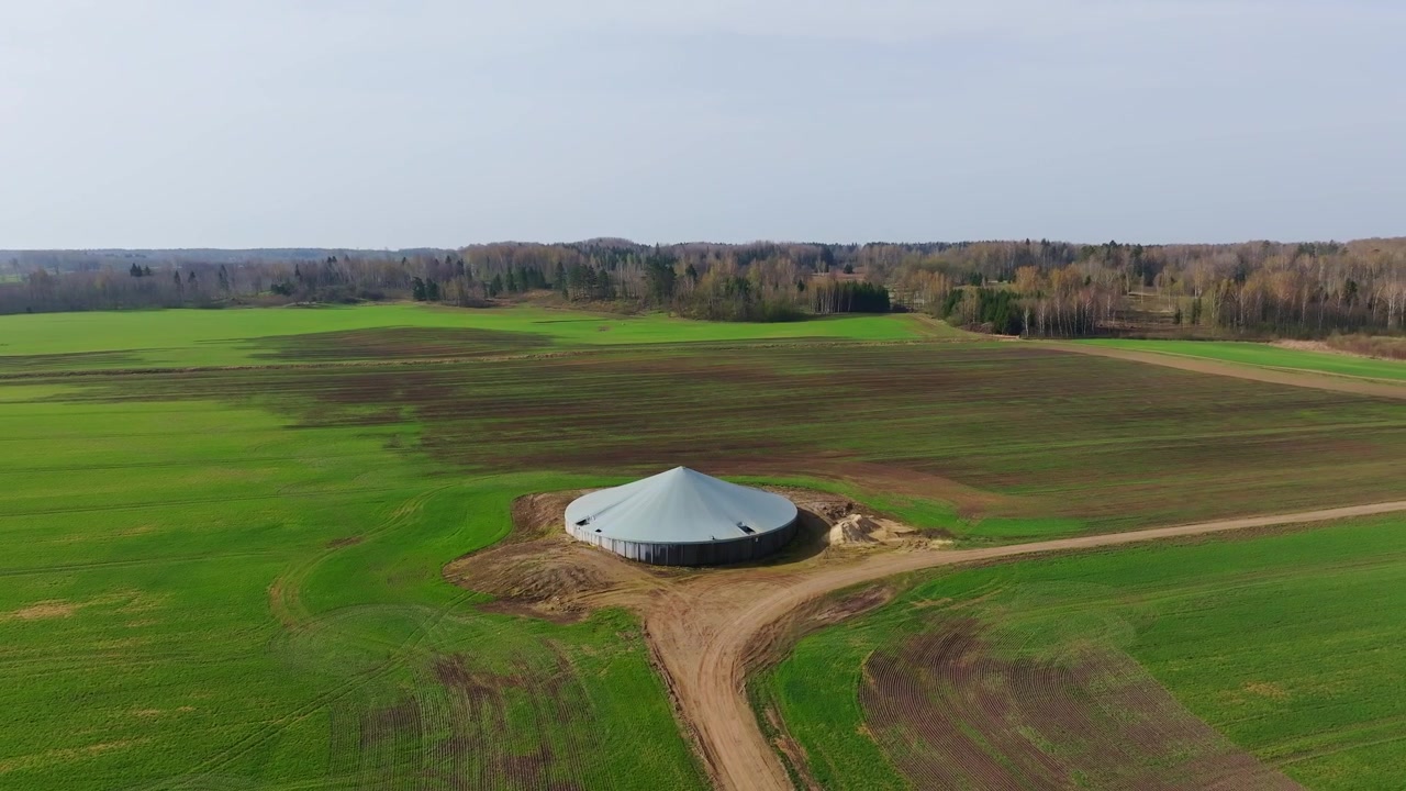 Overdækket landbrugstank står midt blandt frodige forårsafgrøder og dyrkede marker i Letland
