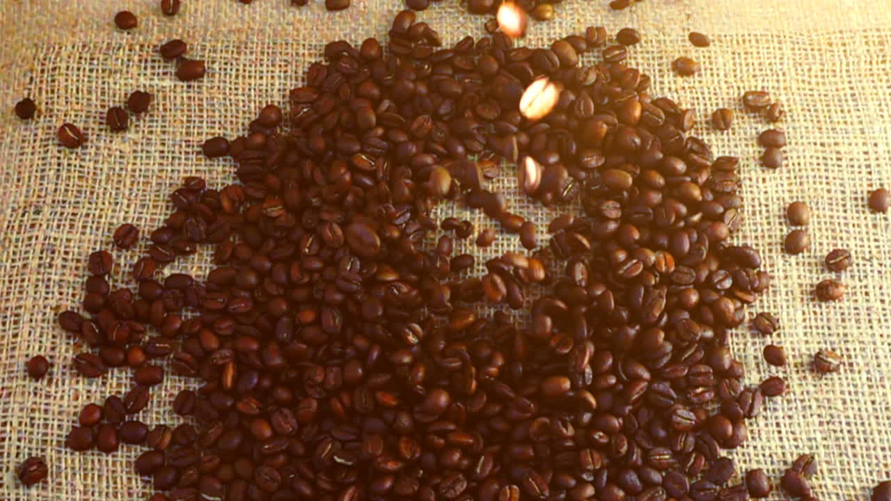 Chicchi di caffè cadono su tela di iuta al rallentatore.
