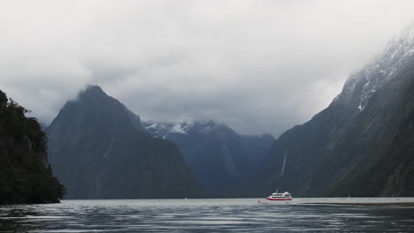un barco parece pequeño rodeado de imponentes acantilados y cascadas muestra la impresionante belleza del estrecho de milford en nueva zelanda