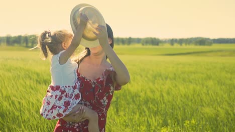 cámara lenta madre joven sostiene a su hija pequeña se paran en un campo verde sonriendo jugando al atardecer