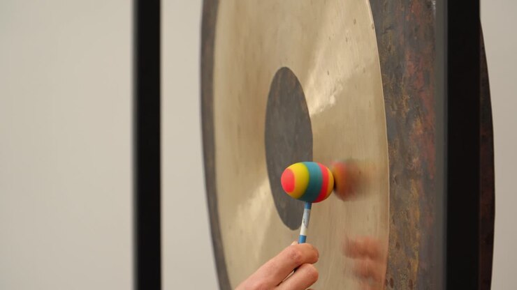 Tight side-detail of silicone friction mallets (flummies) rubbing a large symphonic gong to produce sustained singing tones in a calm minimalist indoor studio