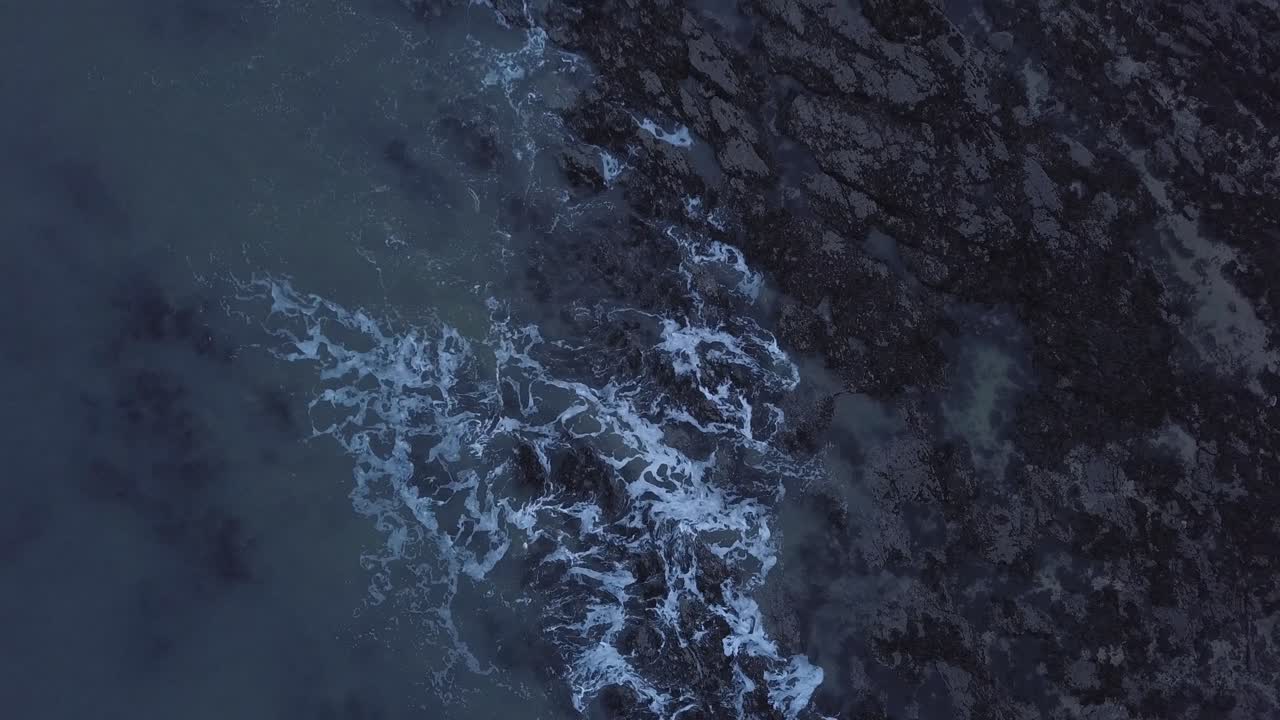 4K drone shot of waves on a rocky winter shore, from a top down angle