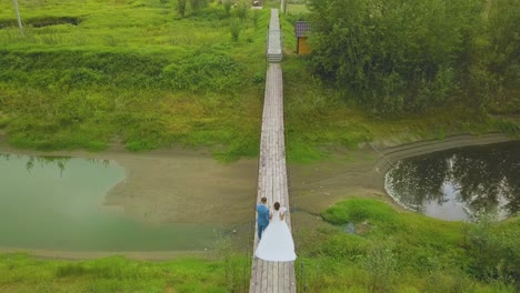 just married couple walks along bridge over stream upper