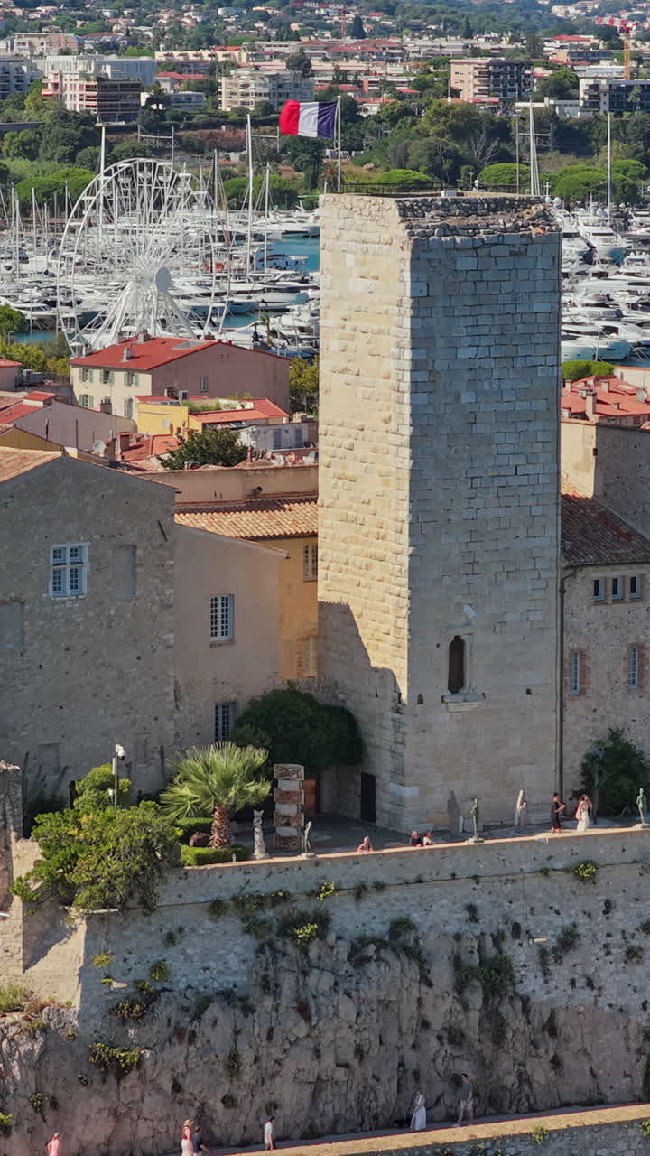 Aerial drone view of the Picasso Museum with its medieval stone towers, overlooking Antibes marina filled with yachts and sailboats. Vertical