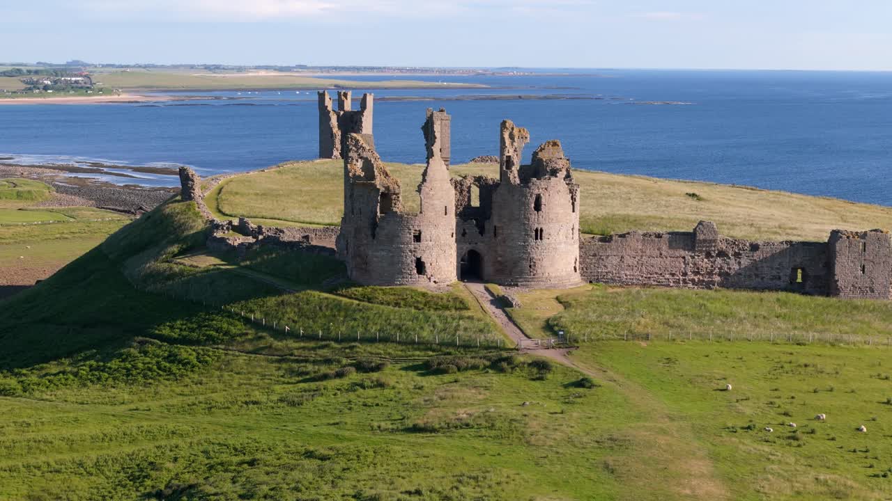 Aerial footage of Dunstanburugh castle ruins on a summer morning with no people