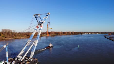 crane ship being pulled by a tugboat across inland river in barendrecht, netherlands