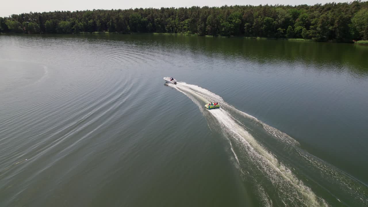 Motorboat pulls Cockpit Tube on a lake, following close drone parallax shot