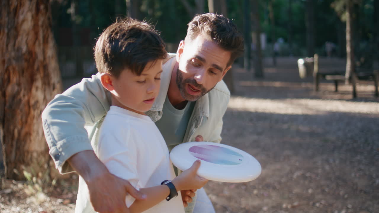 Dad teaching son throwing frisbee plate at forest closeup. Family playing game