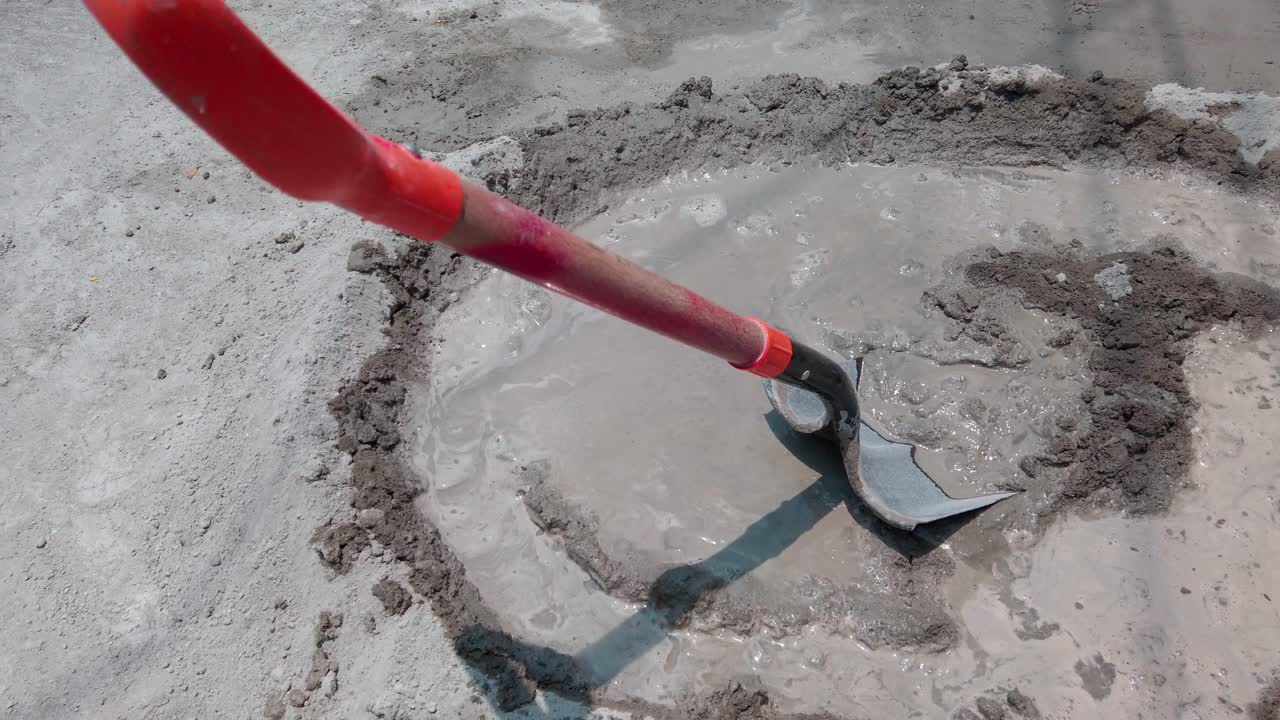 Shovel mixing wet cement by hand on a dusty construction site, work in progress
