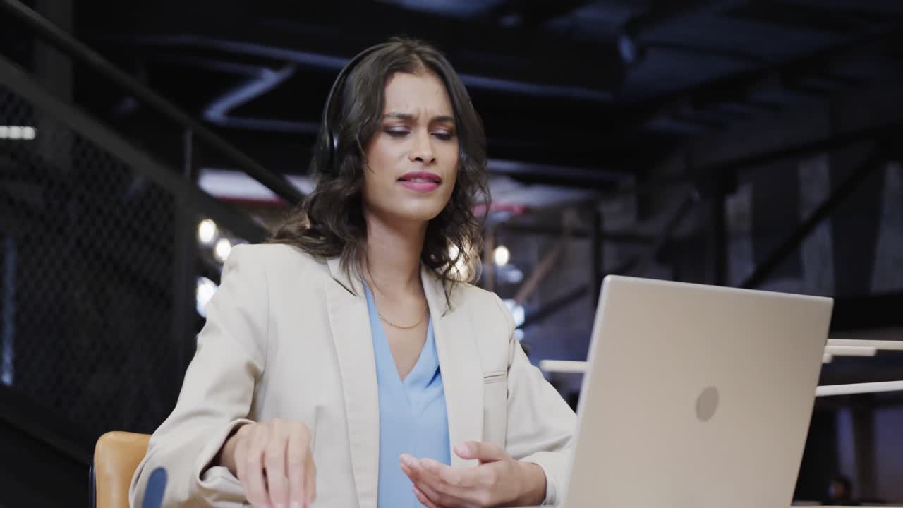 feliz mujer de negocios casual biracial haciendo una videollamada usando una computadora portátil en el salón de la oficina, cámara lenta