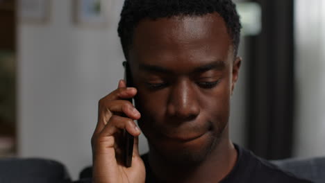 close up of unhappy and depressed young man sitting on sofa at home making call on mobile phone