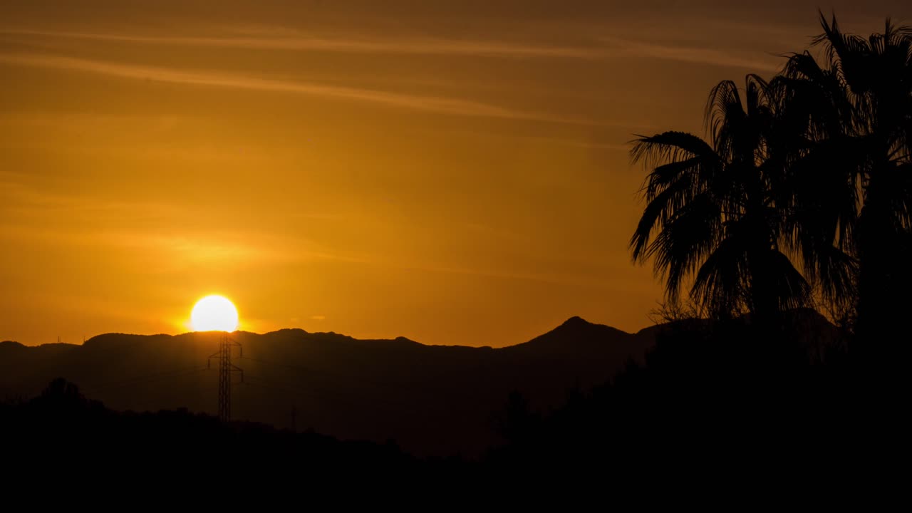 hermoso lapso de tiempo de puesta de sol de 4k filmado con lente de zoom con palmeras en primer plano y puesta de sol detrás de majestuosas montañas en mallorca, españa