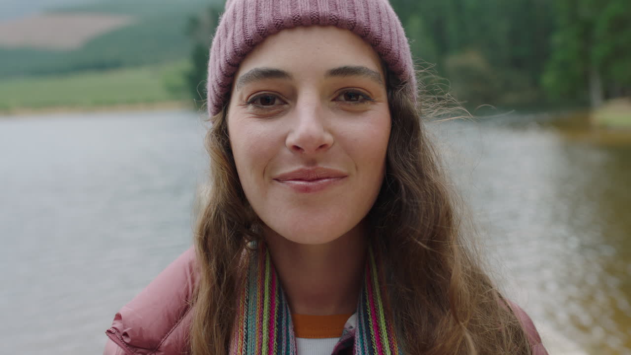 retrato mujer feliz sonriendo sintiendo alegría usando gorro disfrutando del frío invierno al aire libre en la naturaleza junto al lago gente real 4k
