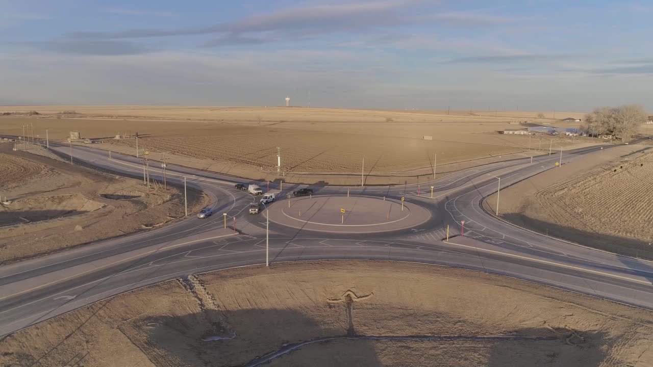 시골 한가운데 있는 원형 교차로, 자동차와 트럭이 원을 천천히 돌아다닙니다.