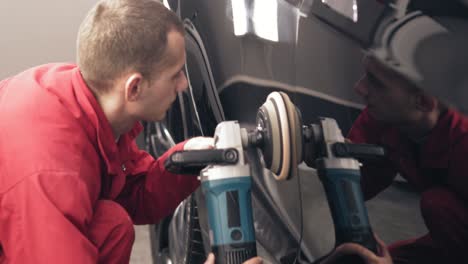 polishing black car with a professional mashine. worker of autocenter in red worksuit is cleaning every millimeter of new tesla car side door.