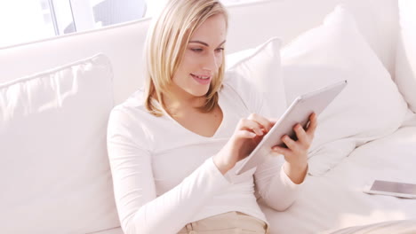 Blonde-Frau-Lächelt-Und-Benutzt-Tablet-Auf-Einem-Sofa