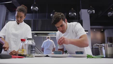cocinero caucásico vestido de blanco en una cocina de restaurante condimentando comida
