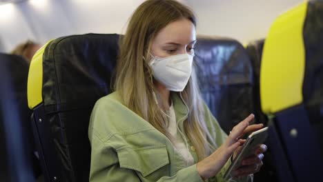 blonde woman in the airplane listen music on earphones using mobile phone during pandemia