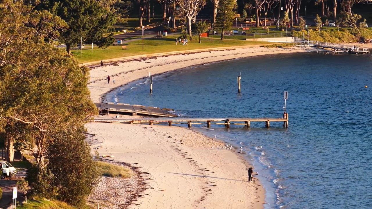Widok z góry na piaszczystą plażę, drewniane molo i tereny parkowe w Nelson Bay w Australii.