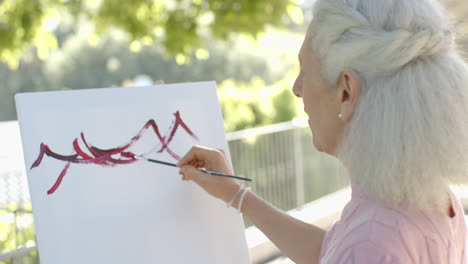 Feliz-Mujer-Birracial-Mayor-Pintando-En-El-Balcón-De-Casa,-Cámara-Lenta