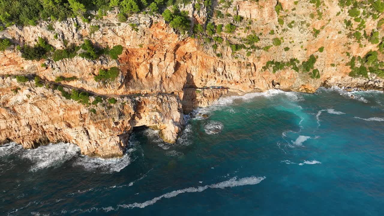 Luftfoto af bølger, der slår mod klipperne nær Dubrovnik, Kroatien, på en lys og klar dag.