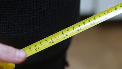 a carpenter man takes a yellow tape measure out of his pocket and measures in feet inches and centimeters