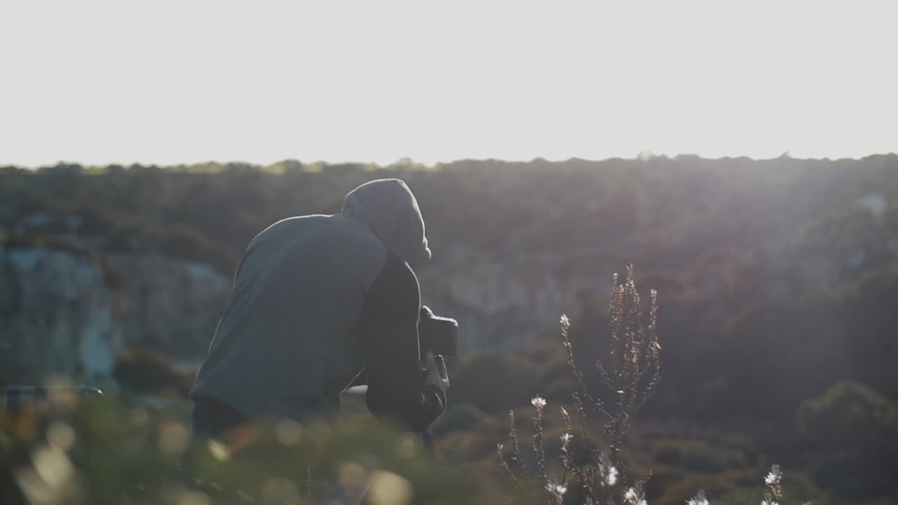 Photographer looks through camera on tripod while sunset to make a picture of the stunning landscape in Mallorca, Spain - Slow Motion
