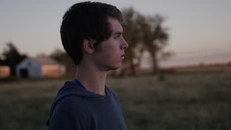 plano lateral medio de un joven adolescente viendo la puesta de sol en un campo de kansas
