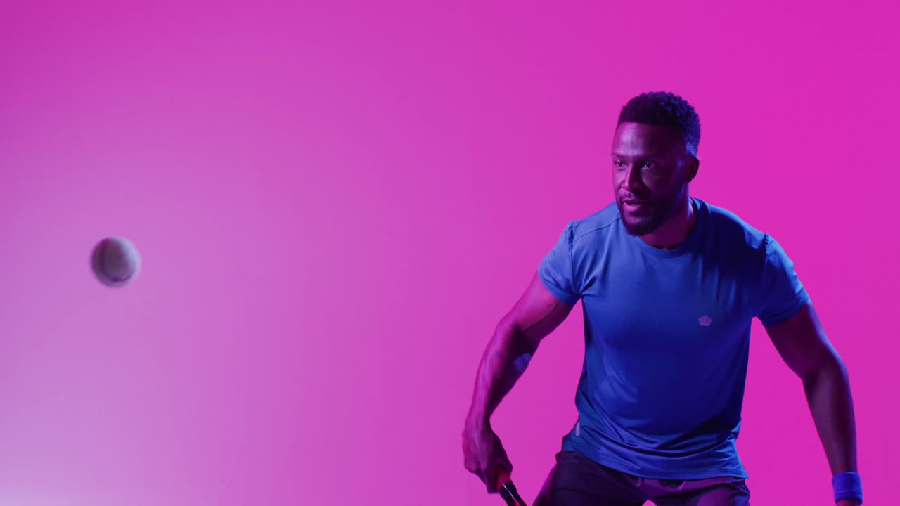 Vídeo de um tenista homem afro-americano bem-sucedido rebatendo a bola em iluminação rosa neon