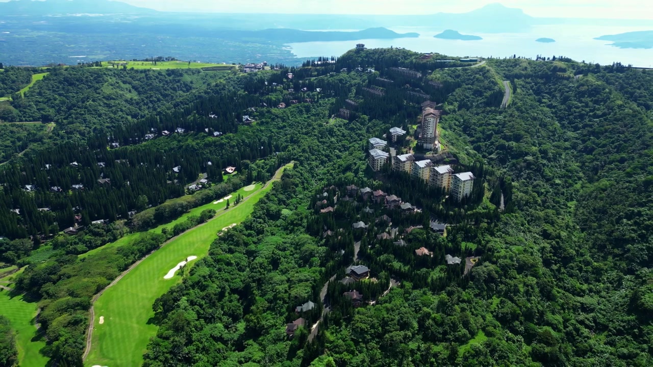 Lüks tatil köyü Tagaytay Highlands projelerini, tropikal ormanları, kıvrımlı dağ yollarını ve Taal Gölü üzerinden Taal Yanardağı'na doğru panoramik manzaraları vurgulayan geniş açılı havadan çekim