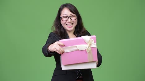 mature beautiful asian businesswoman looking surprised while opening gift box