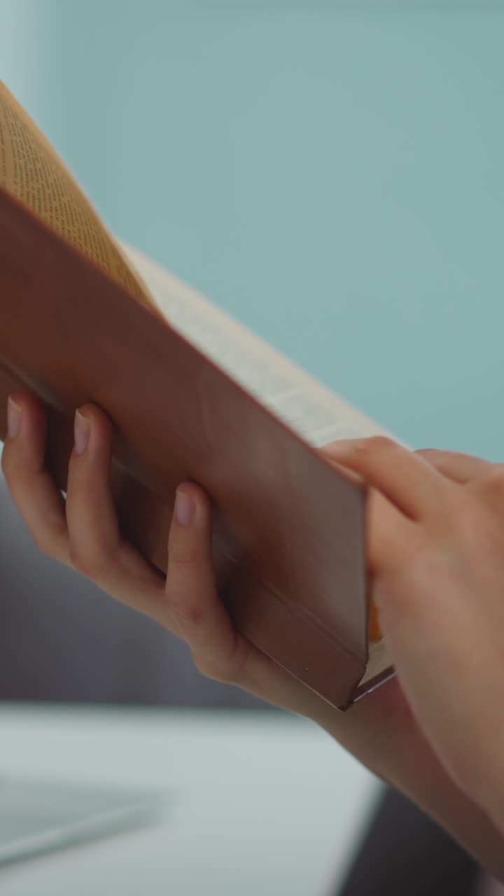 Hands of woman holding book flipping pages on blurred background. Female student reads textbook to find information for report closeup