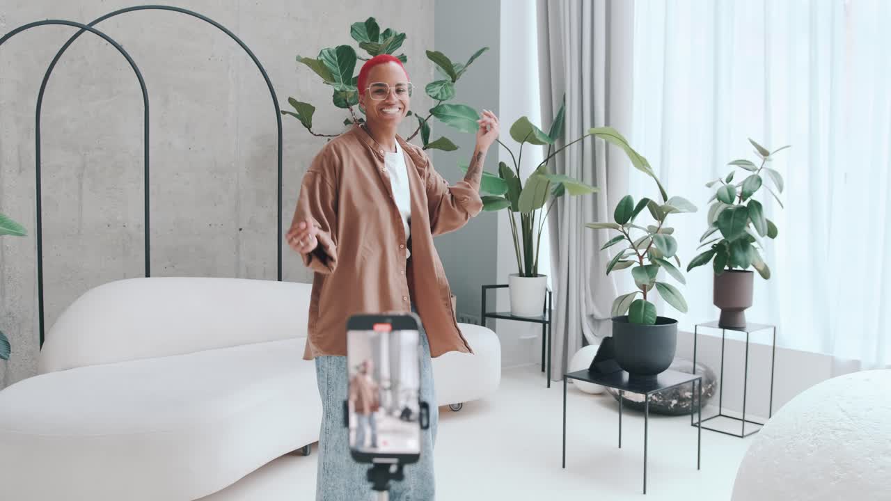 Young african american woman blogger puts smartphone with camera and dancing