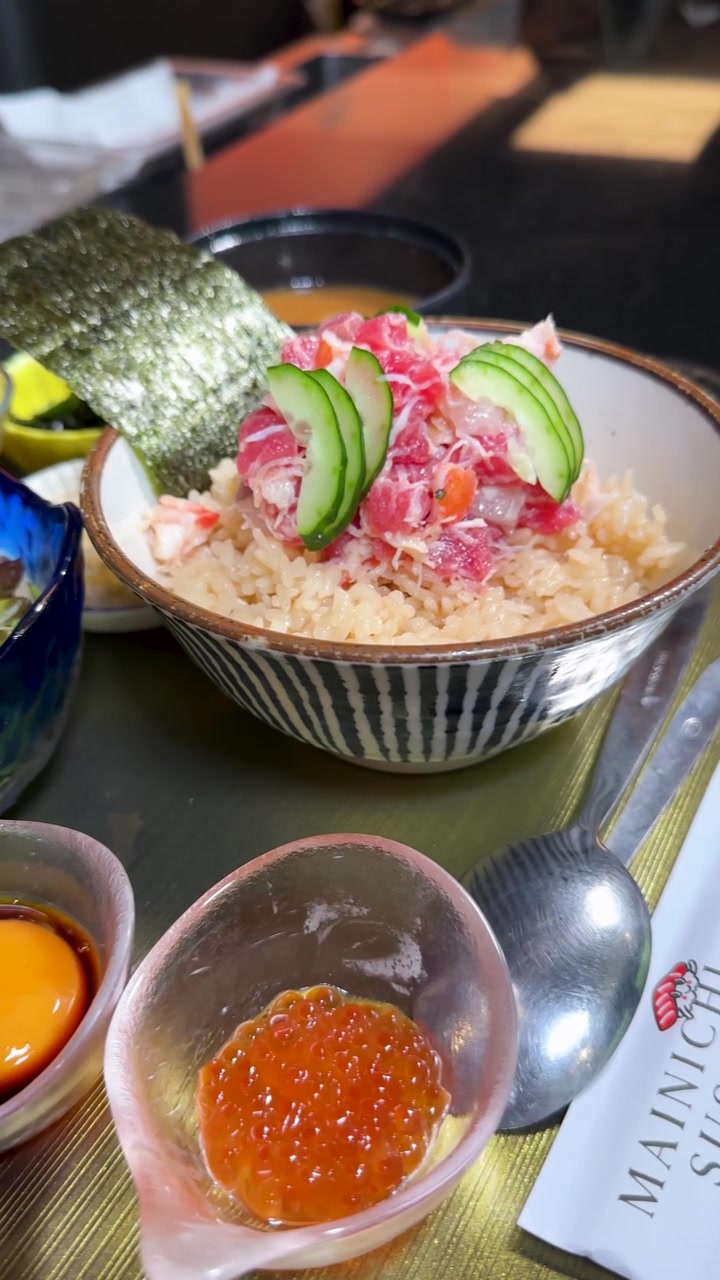 Seorang koki menyajikan semangkuk hidangan laut tradisional Jepang dengan ikan mentah, salad, dan kuning telur.