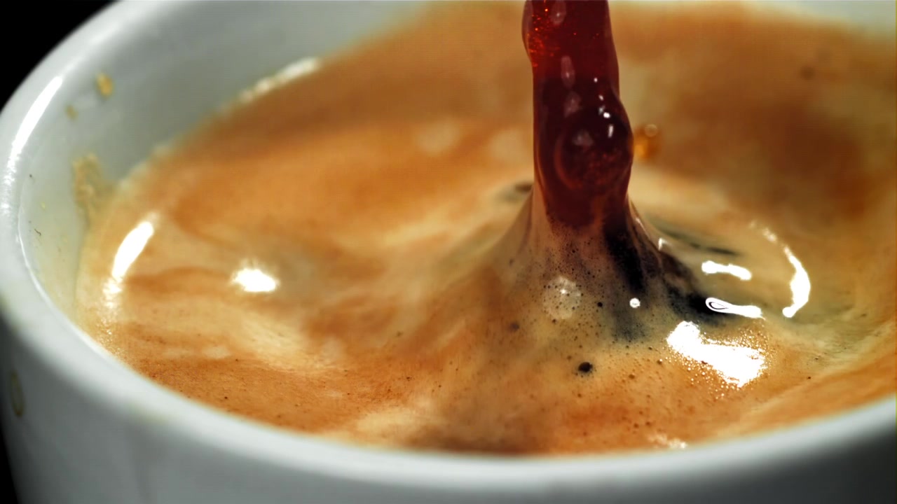 Chicco di caffè in movimento rallentato che cade nella tazzina di espresso