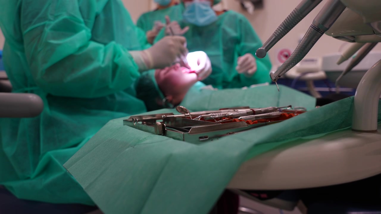 Odaklanmış dişçilik aletleri, arka planda greftleme ameliyatı yapan diş hekimleri.